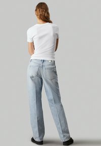 Jeans din denim albastru deschis, cu o croială relaxată, cusături vizibile, două buzunare laterale, purtate cu un top alb strâmt cu mânecă scurtă.