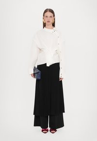 Fehér, gombos blúz drapírozott fazonnal, fekete, plisszírozott maxi szoknyával párosítva. Kiegészítők között egy kék clutch táska és bordó pántos szandálok találhatóak.