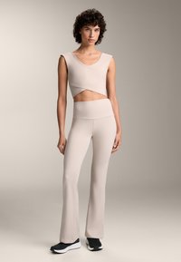 Beige crop top, összecsukható dizájnnal és rövid ujjakkal, magas derekú, harangszárú leggingsszel párosítva, mindkettő sima, rugalmas anyagból készül. 