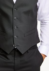 Gilet formale nero realizzato in un tessuto testurizzato con sei bottoni e doppie tasche laterali, abbinato a una camicia bianca.