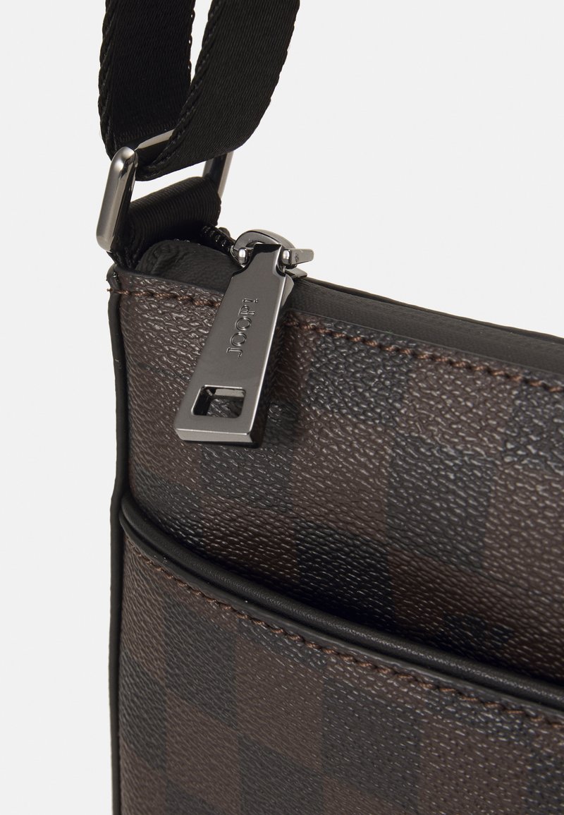 Brązowa, w kratkę torba na ramię z teksturowanym wykończeniem, metalowym uchwytem suwaka oraz regulowanym paskiem. Posiada kontrastowe szwy i elegancki design.