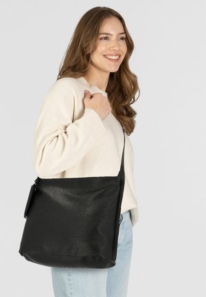 Schwarze Leder-Schultertasche mit einer glatten, strukturierten Oberfläche und einem einzelnen Schultergurt, lässig zu einem hellen Outfit getragen.