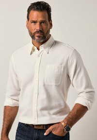 Wit overhemd met knopen van zachte, textuurrijke stof en een borstzakje. Voorzien van opgerolde manchetten en een klassieke kraag. Draagt het met een donkere spijkerbroek en een horloge.