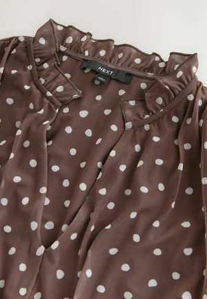 Braune Bluse mit weißen Polka-Dots, versehen mit einem gerafften Kragen und einem weichen, transparenten Stoff. Enthält ein Etikett mit der Aufschrift "NEXT" auf der Innenseite.