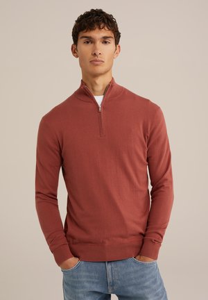 Pullover rouille à manches longues avec un col zippé mi-haut, fabriqué en tissu doux. Design ajusté avec des poignets et une taille côtelés.