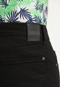 Czarne dżinsy z denimu z skórzaną naszywką z wytłoczonym napisem "Pioneer", akcentującym ściegem oraz metalowymi elementami przy kieszeniach.