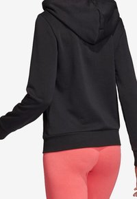 Sweat-shirt noir à capuche avec manches longues, doté d'une texture douce et d'un ourlet côtelé. Porté avec des leggings rose vif pour le contraste.