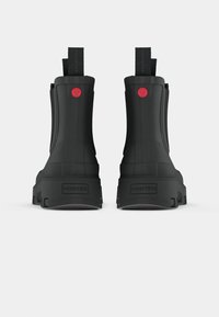 Botas de tobillo de goma negra con una superficie texturizada, que presentan un detalle de logo rojo y tiradores en la parte trasera para facilitar su uso. Diseño de suela plana.