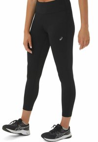 Black leggings made of stretchy material, featuring a high waistband and a small logo on the thigh, worn with black athletic shoes.