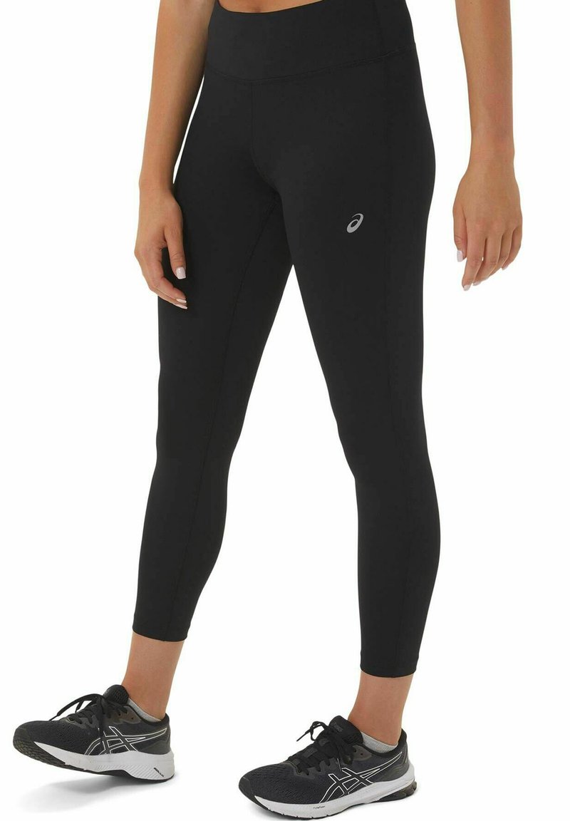 Black leggings made of stretchy material, featuring a high waistband and a small logo on the thigh, worn with black athletic shoes.