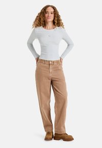 Camisa de manga larga a rayas en azul claro y blanco; pantalones de pana tan con un corte relajado; zapatos marrones con cordones y suela texturizada.