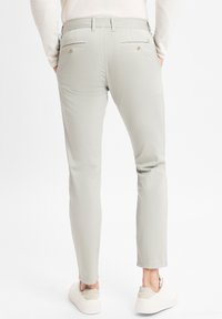Hellgraue Hose mit Slim-Fit, ausgestattet mit zwei Gesäßtaschen mit Knöpfen und einer glatten, matten Textur. Getragen mit weißen Sneakers.