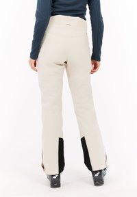 Lichtbeige skibroek met een gestructureerde tailleband, zwarte accenten bij de boord en open ritsen voor ventilatie bij de enkel.