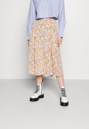 Person wearing a blue striped shirt, floral midi skirt, and white lace-up combat boots standing against a plain light background.