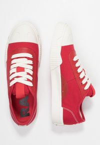 Baskets en toile rouges avec des lacets blancs, semelles en caoutchouc et accents contrastants. Bout arrondi et détails cousus sur les côtés.