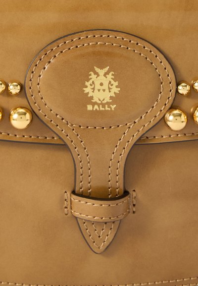 Sac en cuir tan avec des clous et des accessoires dorés, un fermoir décoratif et un logo en relief avec des détails cousus.