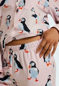 Rosa pyjamaset med puffin-mönster; toppen har en ficka och byxorna har resårmidja. Mjukt tyg med slät textur.