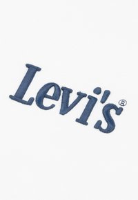 Μπλε κεντημένο λογότυπο "Levi's" σε λευκό υφασμάτινο φόντο, με καθαρή και διακριτή γραμματοσειρά με στρογγυλεμένες άκρες και σύμβολο καταχωρημένου εμπορικού σήματος.