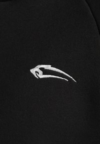 Sort stof med en glat tekstur pryder et hvidt broderet logo, der ligner en stiliseret fugl i flugt, placeret på venstre side.