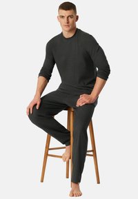 Mørkegrå loungewear sæt med en langærmet skjorte og matchende bukser, lavet af blødt stof, med et enkelt, tætsiddende design.