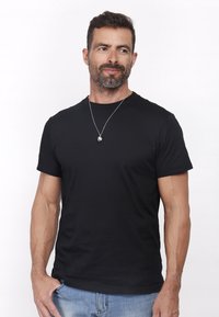 Sort kortærmet T-shirt i bomuld med rund halsudskæring og tætsiddende silhuet. Bæres med en sølv halskæde.