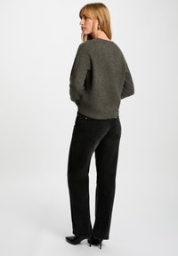 Suéter de punto gris oscuro con un escote amplio, combinado con jeans negros de cintura alta y tacones puntiagudos negros. Tejido texturizado, ajuste relajado.