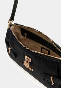 Czarna torebka Guess z fakturowanej skóry, z złotym zapięciem, beżową podszewką, kieszenią na zamek i odpinanym paskiem na ramię.