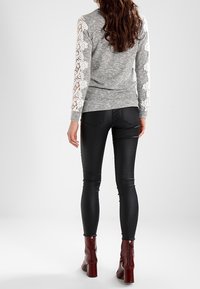 Grå tröja med lång ärm som har vit spetsdetaljering. Svarta tights och vinröda klackstövlar fulländar outfiten.