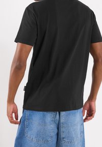 Camiseta de algodón negra de manga corta y corte regular, combinada con pantalones cortos de denim azul con grandes bolsillos traseros y un diseño relajado.