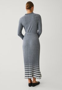 Graues geripptes Midi-Kleid mit langen Ärmeln, tailliertem Schnitt und Rüschenausschnitt. Der gestreifte Saum zeigt abwechselnd graue und weiße Muster.