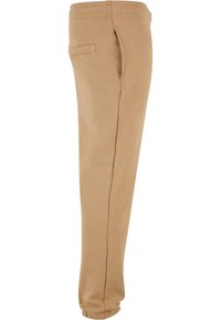 Beige Sweatpants mit elastischem Bund, seitlichem Taschen, schmal zulaufenden Beinen und einer weichen, glatten Textur. Einfaches Design ohne Muster.