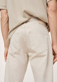 Pantalones de mezclilla beige con un diseño de pierna recta, que cuentan con dos bolsillos traseros y un tejido suave y texturizado. Costuras visibles y detalle en la cinturilla.