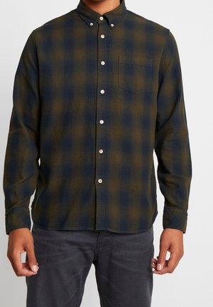 Chemise en flanelle à carreaux verts foncés et bleu marine. Dotée d'un col boutonné, d'une poche avant et de boutons blancs. Tissu doux et texturé.