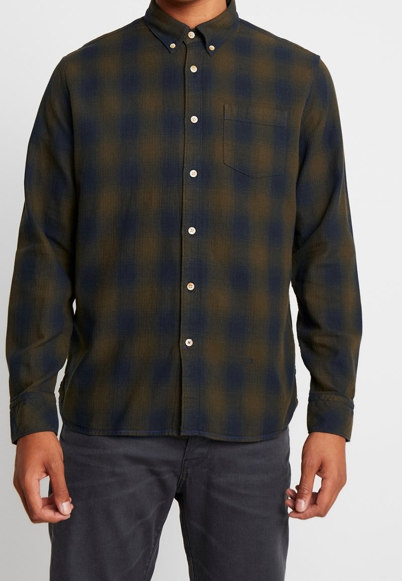 Camicia in flanella a quadri verde scuro e blu navy. Caratterizzata da un colletto button-down, una tasca frontale e bottoni bianchi. Tessuto morbido e testurizzato.