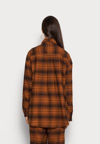 Camicia di flanella a scacchi arancio e nera, caratterizzata da una vestibilità comoda, maniche lunghe e polsini con bottoni. Tessuto morbido con colletto.