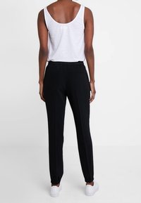 Pantalon de jogging noir à taille élastique avec ourlets côtelés, associé à un haut sans manches blanc. Tissu lisse et design simple, adapté pour une tenue décontractée.