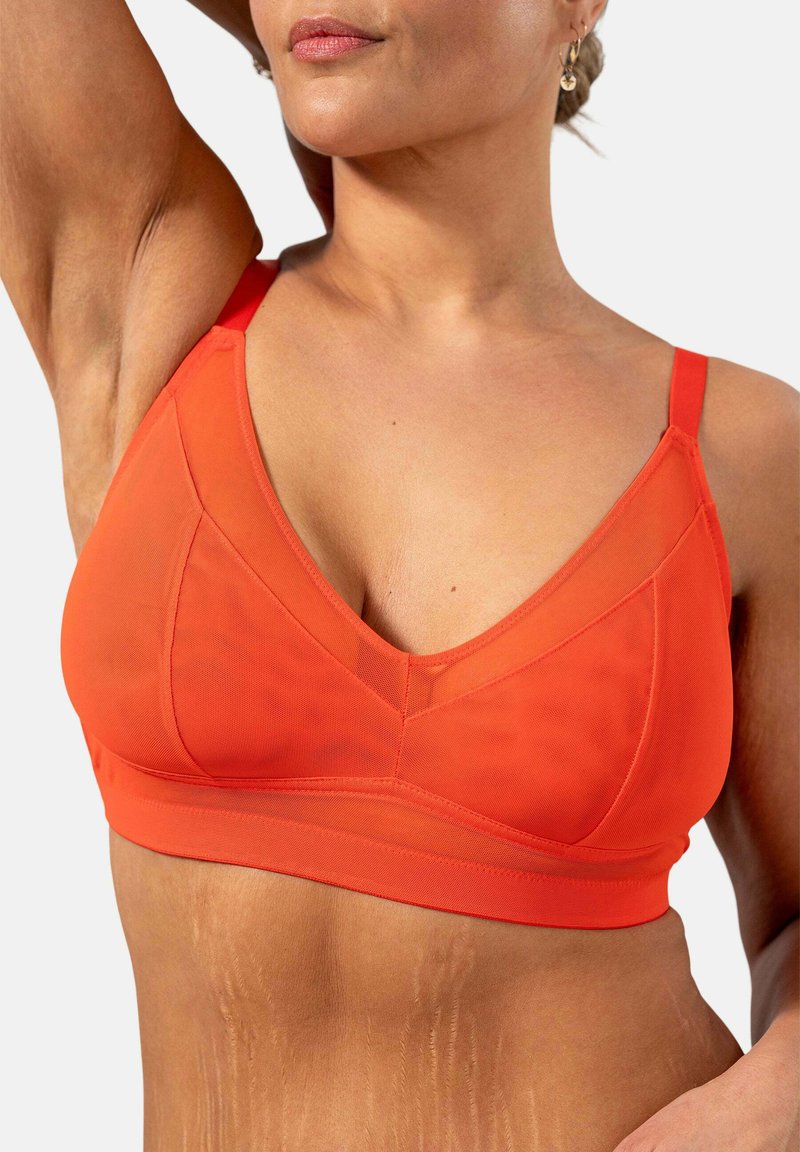 Punainen bralette V-aukolla, joka on valmistettu sileästä ja kevyestä kankaasta. Ominaisuuksiin kuuluvat säädettävät olkaimet ja saumaton vyötärönauha tukemista varten.