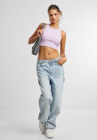 Lyselilla kroppet tanktop, lyseblå baggy jeans og hvite joggesko. Modellen bærer en grå veske; tekstur og design er uformelt og avslappet.