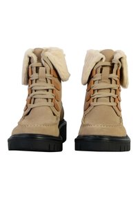 Stivali in suede beige con una soffice cintura crema, occhielli rinforzati, lacci marroni e una robusta suola nera in gomma. Il design bicolore mette in risalto la texture.