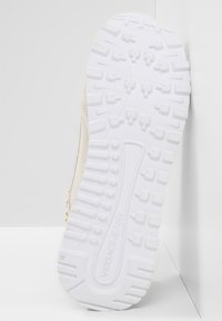 Semelle d'une sneaker avec une semelle extérieure en caoutchouc blanc texturé, présentant des rainures profondes et des motifs circulaires, brandée "VERSACE JEANS" de manière proéminente.