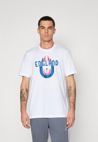 Hvid bomulds t-shirt med blå og rød "ENGLAND" grafik i et cirkulært design. Korte ærmer og klassisk rund hals.