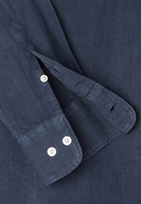 Camicia di lino blu navy scuro con maniche lunghe, bottoni bianchi e polsini con bottone. Presenta una texture visibile e dettagli cuciti.