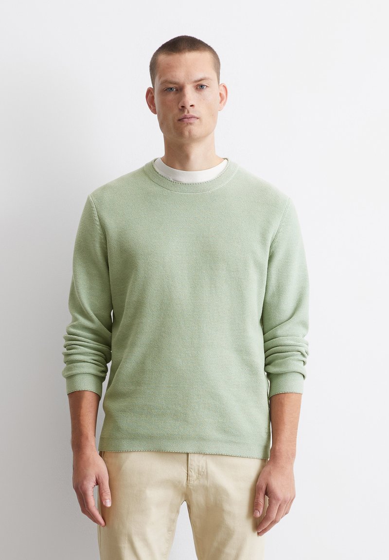 Hellgrüner, strukturiertes Sweatshirt mit Rundhalsausschnitt und langen Ärmeln, kombiniert mit hellen Hosen. Einfache und klassische Gestaltung.