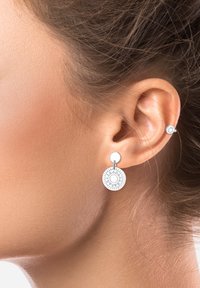 Boucles d'oreilles pendantes en argent avec des pendentifs circulaires et texturés ornés de motifs solaires. De petites boucles d'oreilles à clou accompagnent la pièce principale.