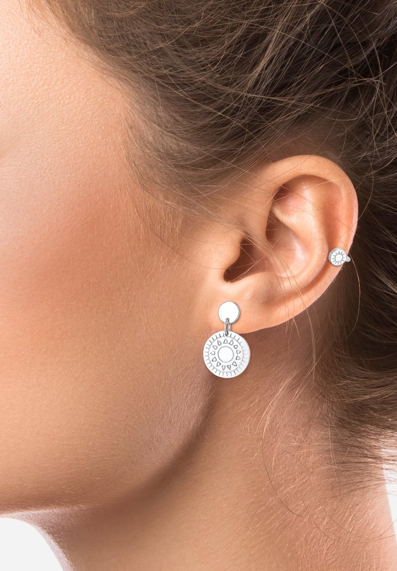 Boucles d'oreilles pendantes en argent avec des pendentifs circulaires et texturés ornés de motifs solaires. De petites boucles d'oreilles à clou accompagnent la pièce principale.