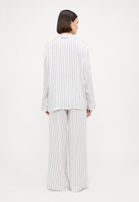 Pajama set s dugim rukavima i širokim hlačama s bijelim prugama. Sadrži vertikalne pruge u kontrastnoj boji.