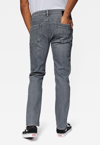 Jeans de mezclilla gris con corte ajustado, que cuentan con dos bolsillos traseros, un pasador para cinturón y costuras en contraste. Combinados con zapatillas negras y blancas.