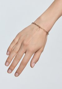 Złota bransoletka z łańcucha z delikatnym charms z koniczyną. Gładka faktura, lekka, elegancko owijająca nadgarstek.