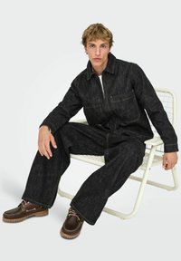 Tume teksariidest kombinesoon kollaste kontrastõmblustega, millel on esikinnis ja kaks rinnataskut. Pruunid paeltega kingad kummist taldadega.