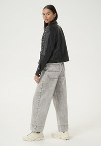Sort læder cropped jakke med nittede detaljer, parret med lysegrå baggy jeans og beige sneakers, der har en afslappet pasform.